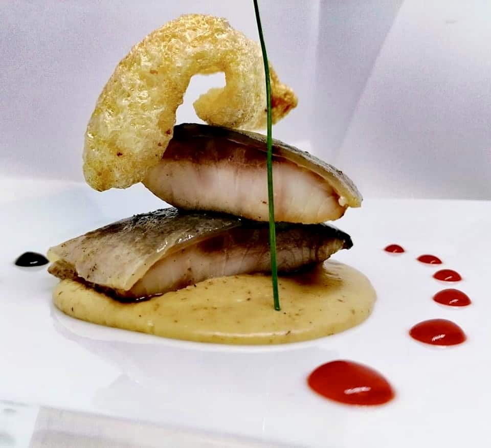 Filetto di pesce impiattato su crema con cialda croccante e gocce di riduzione rossa